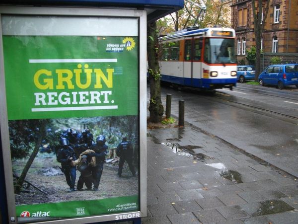 Geadbustetes Plakat mit dem Slogan "Grün Regiert" und einer Szene von Polizeigewalt im Dannenröder Forst
