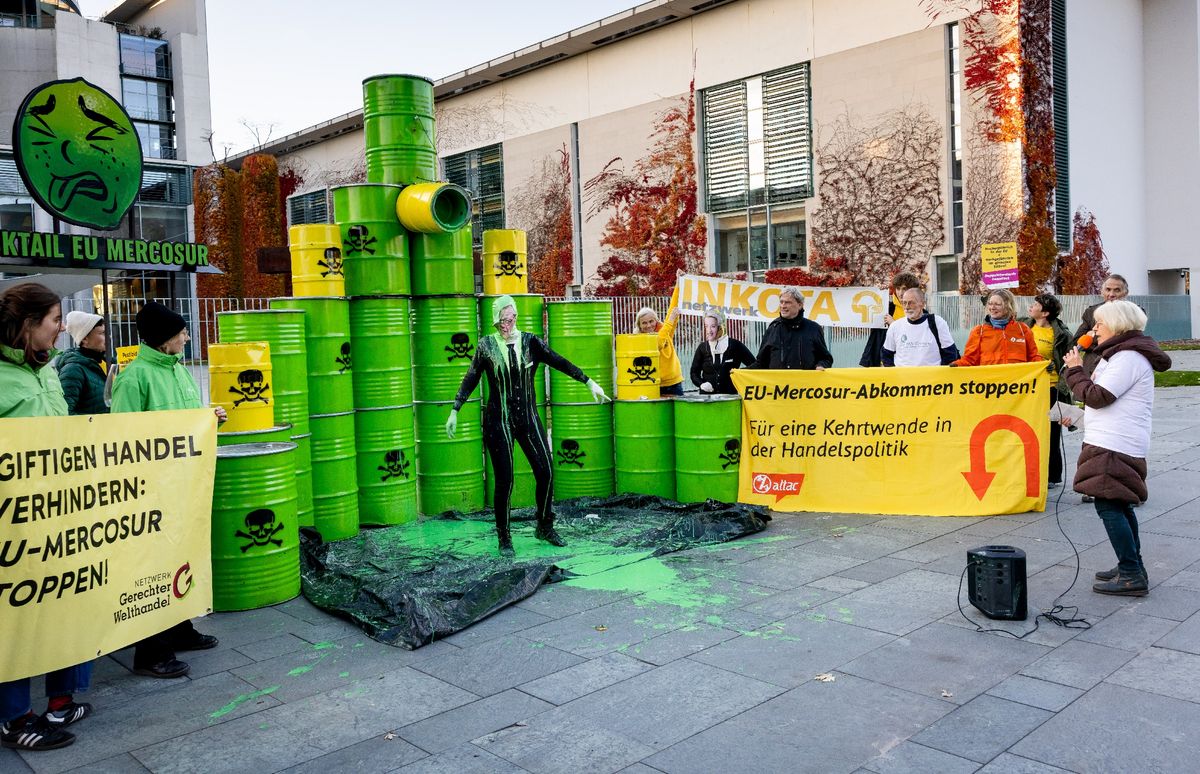 Activisti demonstrieren vor gelben und grünen als Giftfässer markierten Tonnen gegen das EU-Mercosur-Handelsabkommen