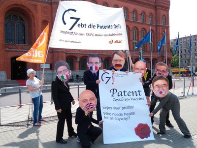 Aktivisti mit Politiker-Masken halten das "Patent für Covid Impfstoff" in ihren Händen. Dahinter wird ein Banner "Gebt die Patente frei! Impfstoff für alle: Trips-Waiver Blockade beenden" und eine Attac-Fahne hochgehalten.