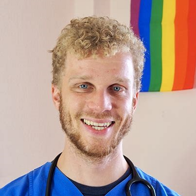 Felix Ahls, Co-Vorsitzender des vdää, lächelnd in blauer Ärzt*innen-Kleidung mit Stethoskop