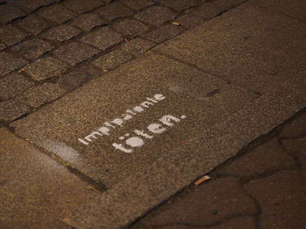Mit einer Sprühkreideschablone steht auf dem Boden  "Impfpatente töten." geschrieben