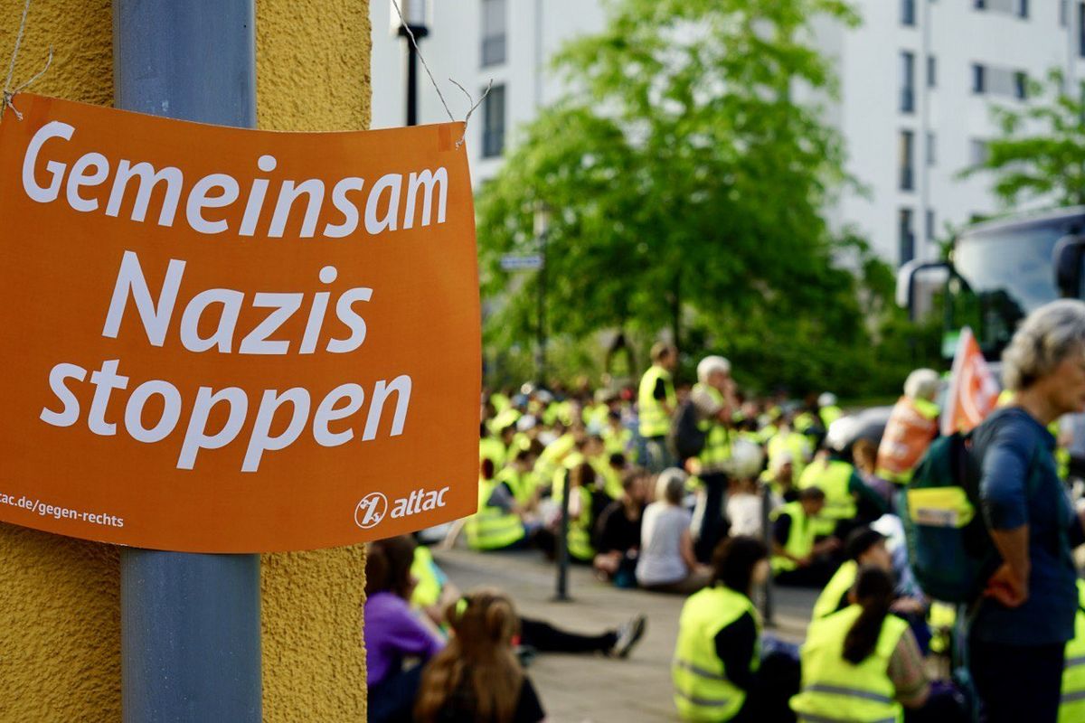 Attac-Plakat "Gemeinsam Nazis stoppen"; im Hintergrund: Sitzblockaden