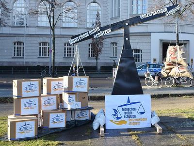 Eine überdimensionale Waage vor dem Wirtschaftsministerium. Darauf links viele Kartons mit Aufschrift "Menschenrechte schützen, Konzernklagen stoppen", rechts mehrere Säcke mit € Zeichen. Die Geldsäcke wiegen leichter und sind oben.