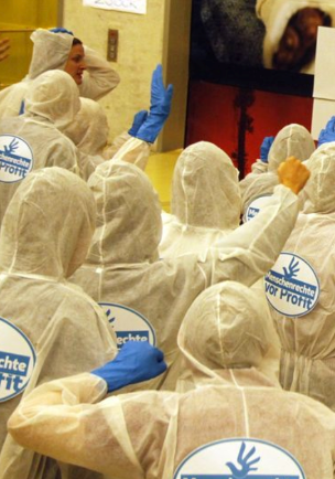 Menschen in weißen Maleranzügen und mit blauen Handschuhen tragen das Kampagnen-Logo auf dem Rücken